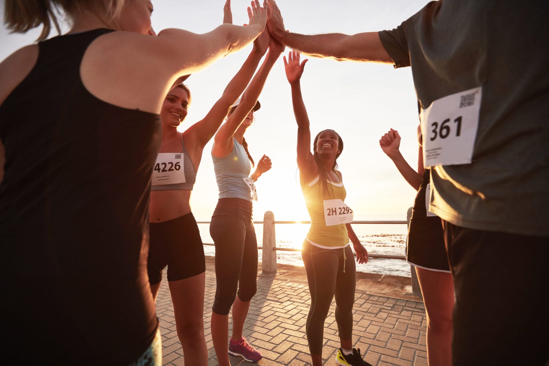 Shot of male and female runners high fiving each other after a race. Diverse group of athletes giving each other high five after winning competition.