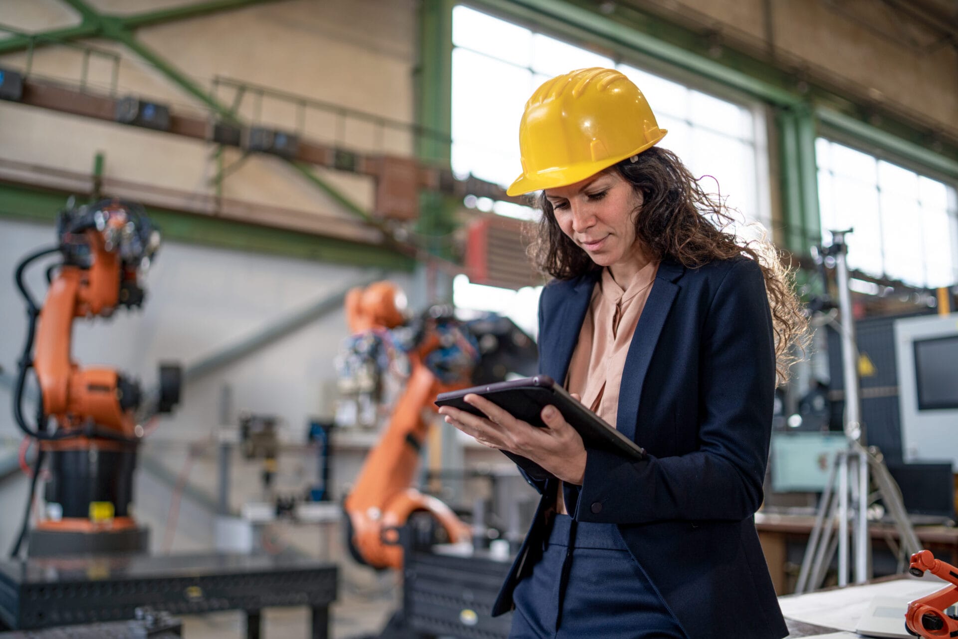 An automation female engineer with tablet for programming robotic arm in factory.