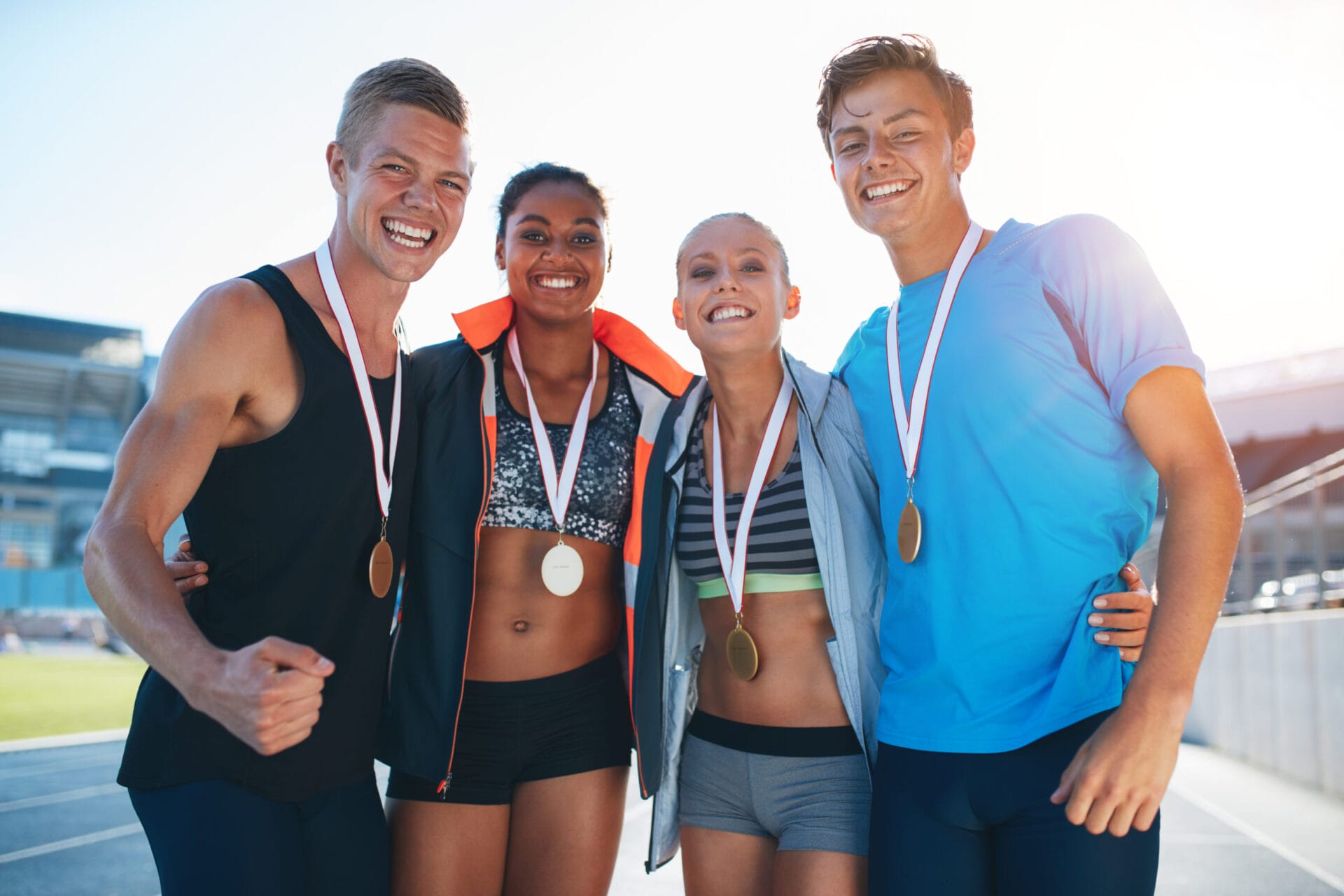 Happy multiracial athletes celebrating victory while standing together on racetrack. Group of runner with medals winning a competition.