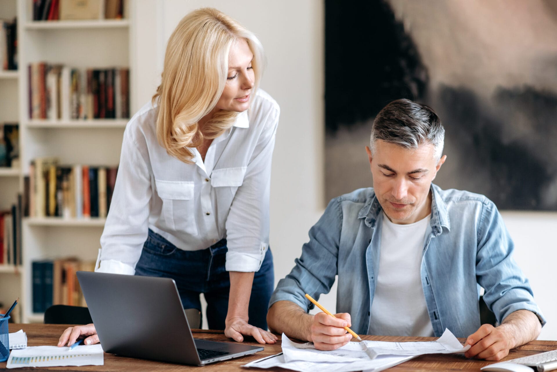 Two successful focused senior caucasian business partners, working together at their workplace in modern office, discussing business schemes and ideas, looking through documents, taking notes