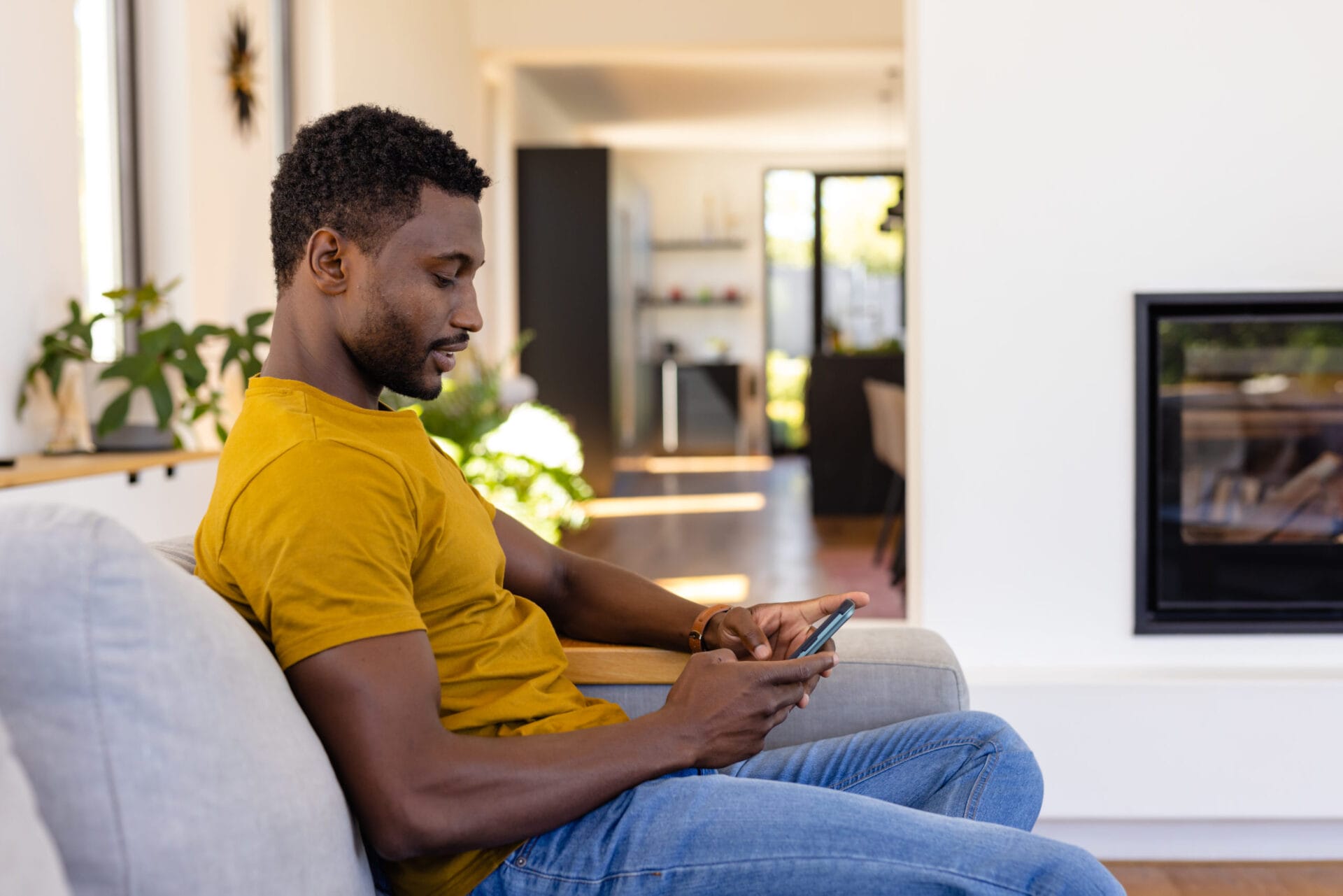 Happy african american man using smartphone in living room. Relaxation, lifestyle, communication and domestic life, unaltered.