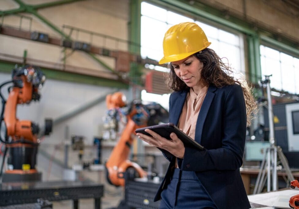 An automation female engineer with tablet for programming robotic arm in factory.