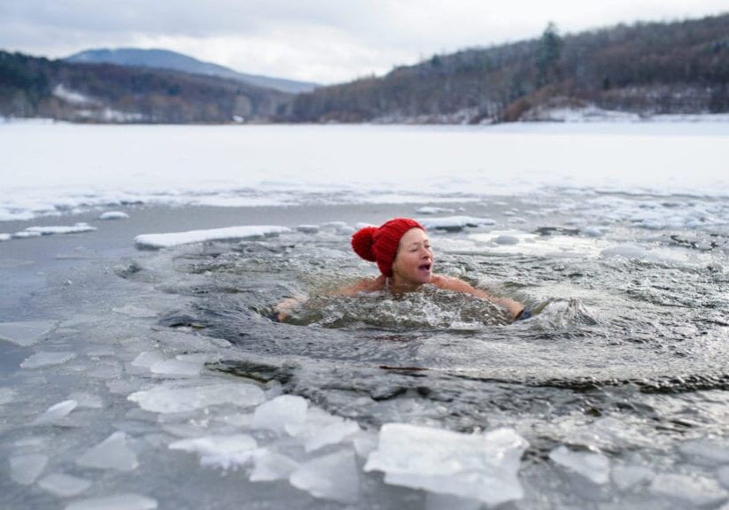 A front view of active senior woman in swimsuit outdoors in water in winter, cold therapy concept.