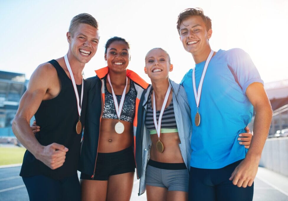 Happy multiracial athletes celebrating victory while standing together on racetrack. Group of runner with medals winning a competition.