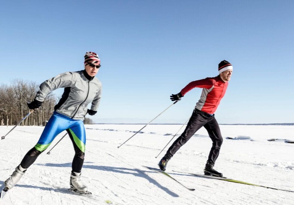 Male and female athletes cross-country skiing on a sunny day.