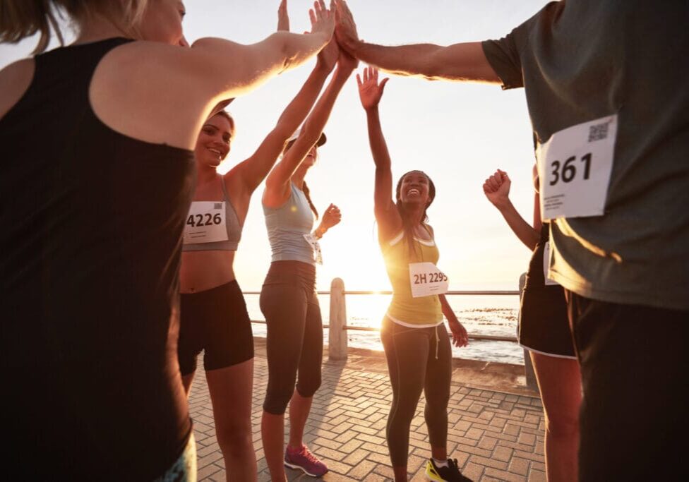 Shot of male and female runners high fiving each other after a race. Diverse group of athletes giving each other high five after winning competition.