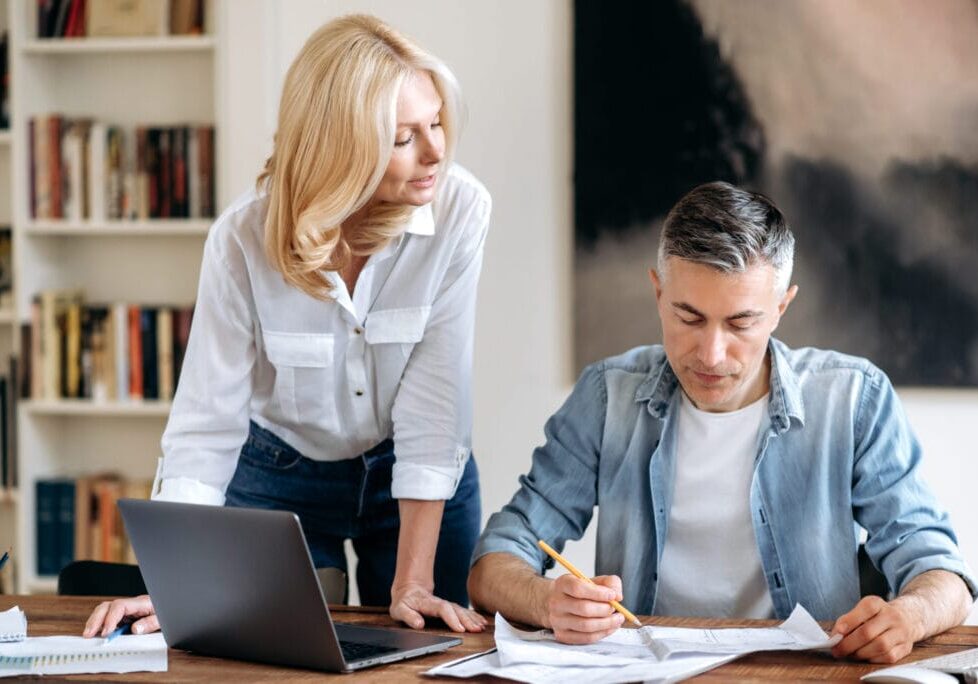 Two successful focused senior caucasian business partners, working together at their workplace in modern office, discussing business schemes and ideas, looking through documents, taking notes